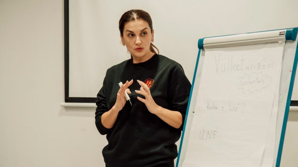 Woman confidently presenting with a flip chart in a classroom setting.